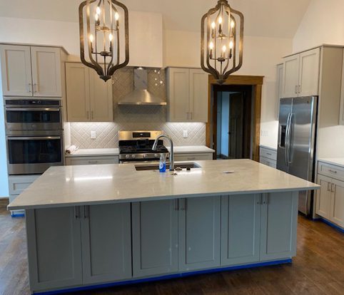 Rice Furniture & Design Center | custom built cabinets and island for kitchen with white backsplash and brass lights